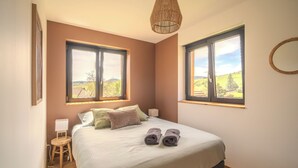 A bedroom with a bed, two windows, a bedside table, a lamp, and a hanging light fixture. - Vrbo Property (Bernardvillé)