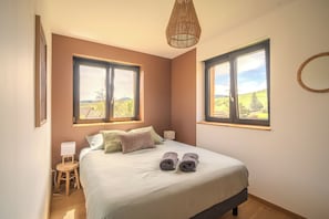 Une chambre à coucher avec un lit, deux fenêtres, une table de chevet, une lampe et un luminaire suspendu.