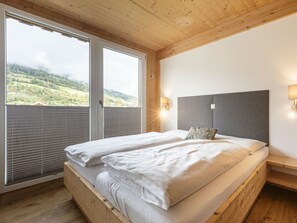 A double bed with a grey headboard in a room with wooden walls and a large window. - Apartment With 1 Bedroom (Sankt Georgen am Kreischberg)