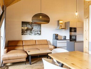 A modern interior with a sofa, a wooden table, a kitchen area, and a pendant light. - Apartment With 1 Bedroom (Sankt Georgen am Kreischberg)