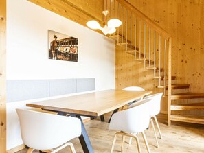 A wooden interior with a long table and two white chairs, a staircase, and a wall-mounted picture. - Apartment With 1 Bedroom (Sankt Georgen am Kreischberg)