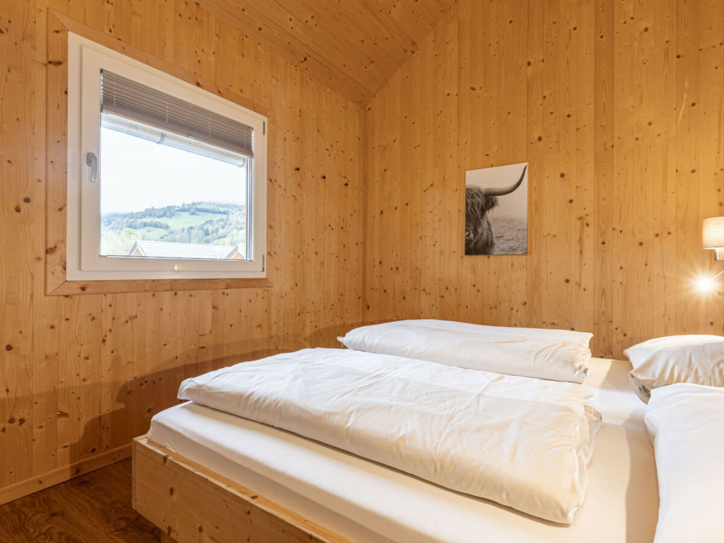 Una stanza con pannelli in legno, un letto, una finestra con persiane e una lampada fissata al muro.