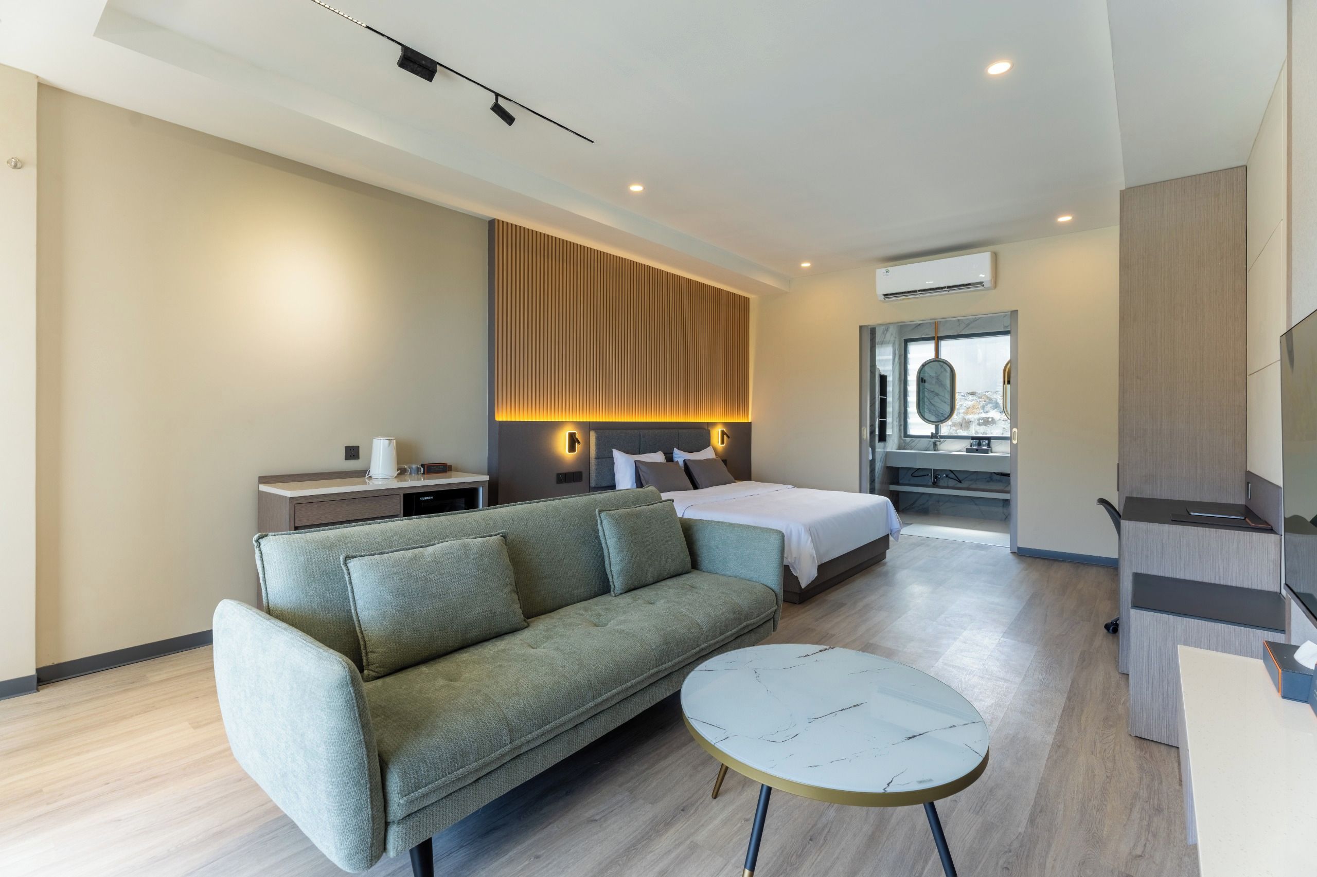 Una habitación de hotel moderna con sofá, una mesa redonda, cama, escritorio y baño con espejo.