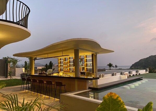 A modern outdoor bar area with a pool, bar stools, and a view of the sea.