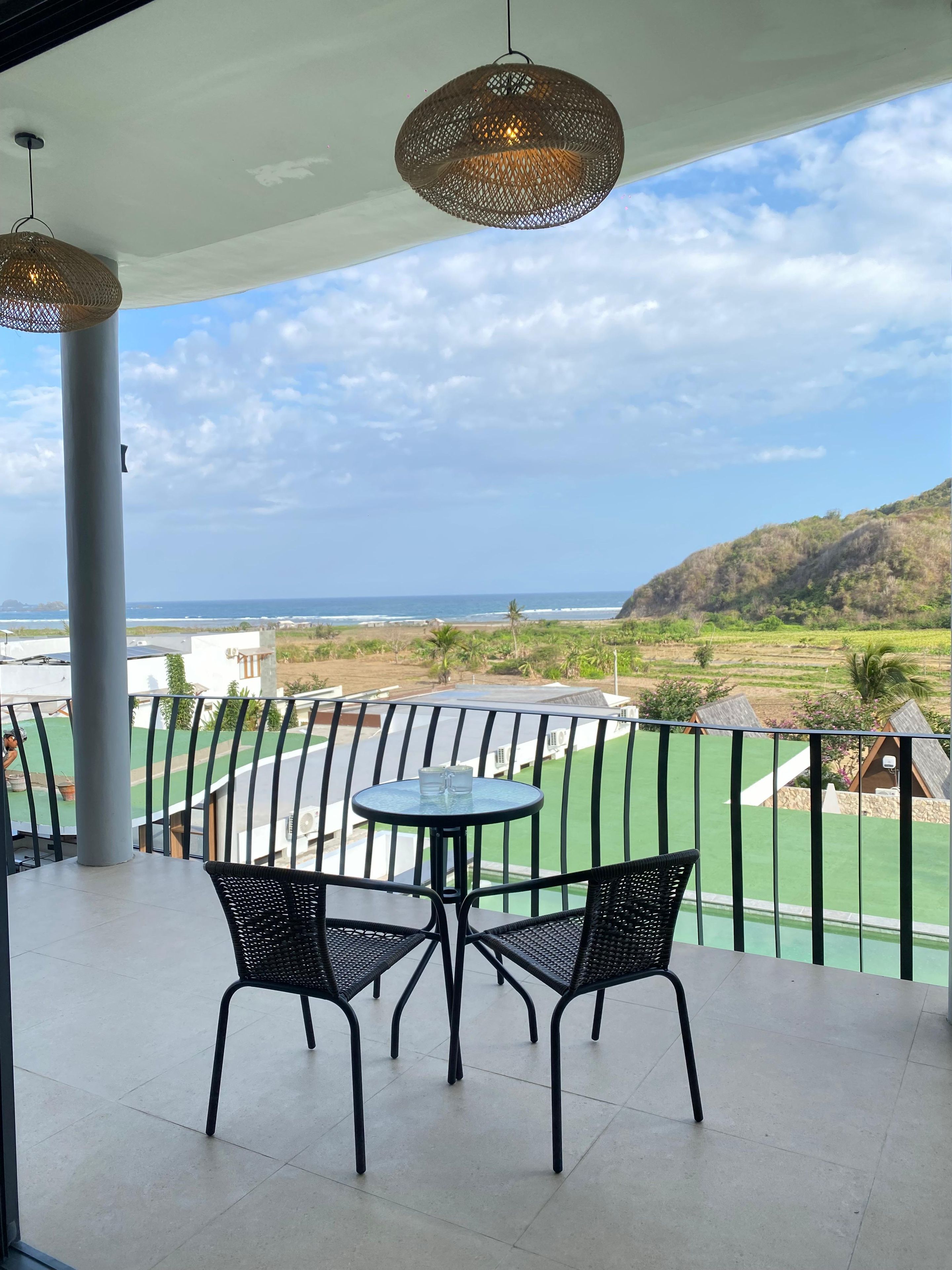 A balcony with a table and chairs, overlooking a beach and green landscape.