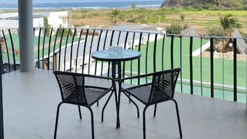 A balcony with a table and chairs, overlooking a beach and green landscape.