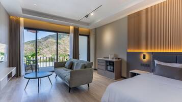 A modern hotel room with a balcony, a sofa, a dining table, a bed, and a small kitchenette.