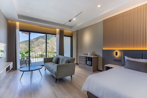 A modern hotel room with a balcony, a sofa, a dining table, a bed, and a small kitchenette. - Tampah Bay Boutique Resort (Kuta)