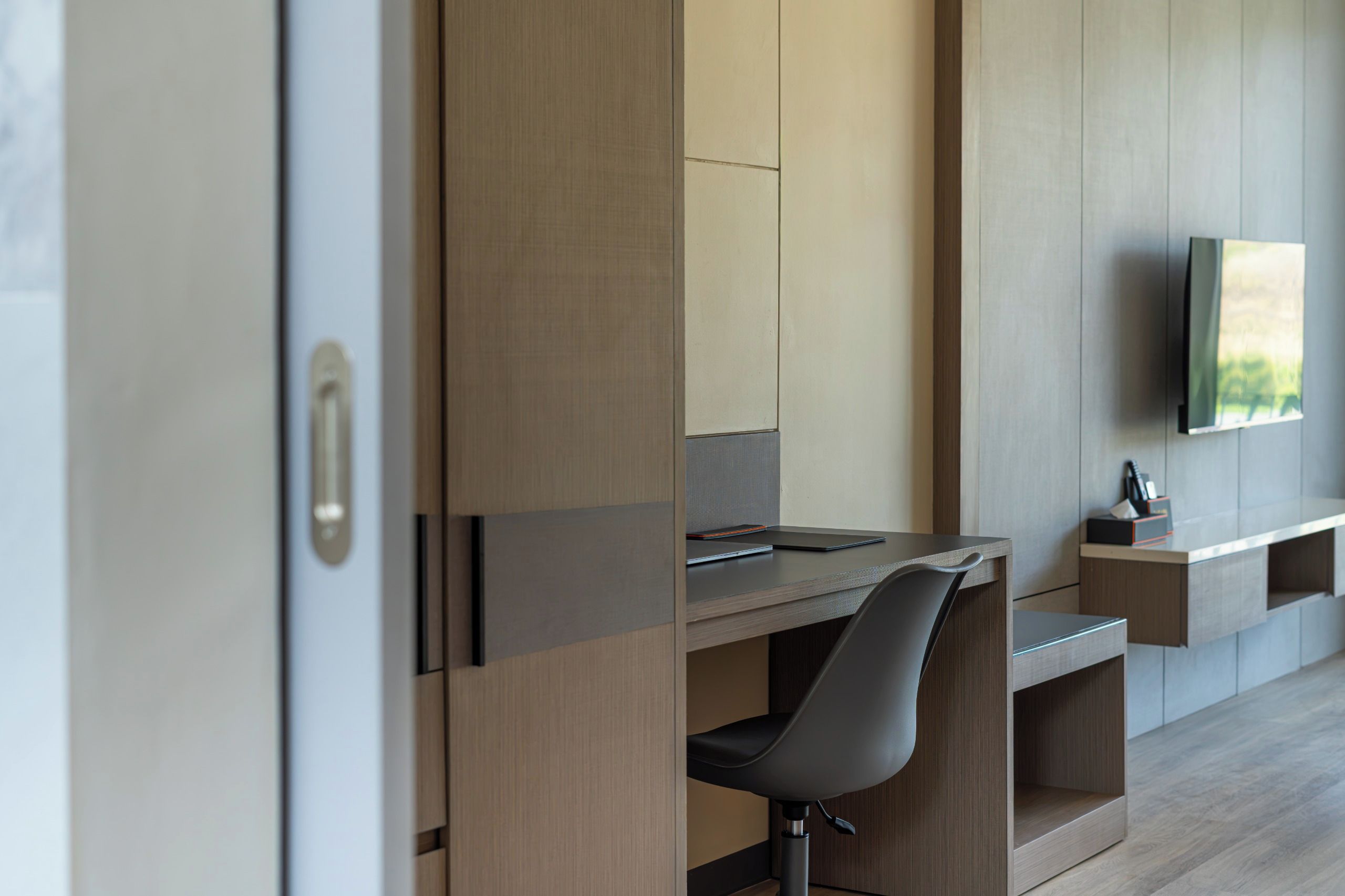 A modern, minimalist room with a built-in desk, a chair, and a flat-screen TV mounted on the wall.
