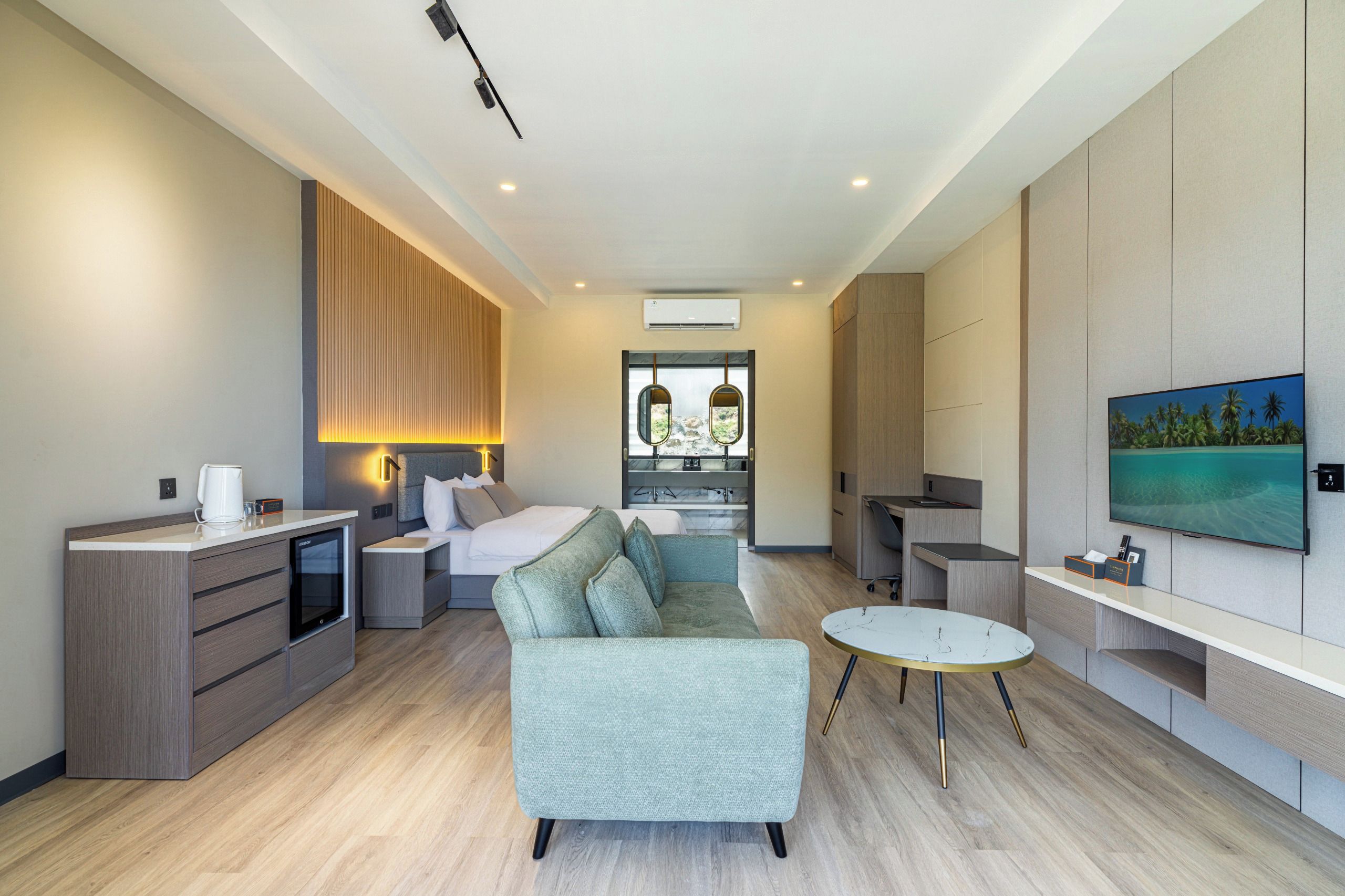Una habitación de hotel moderna con sofá, mesa de comedor, televisor y minibar.