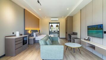 Una habitación de hotel moderna con sofá, mesa de comedor, televisor y minibar.