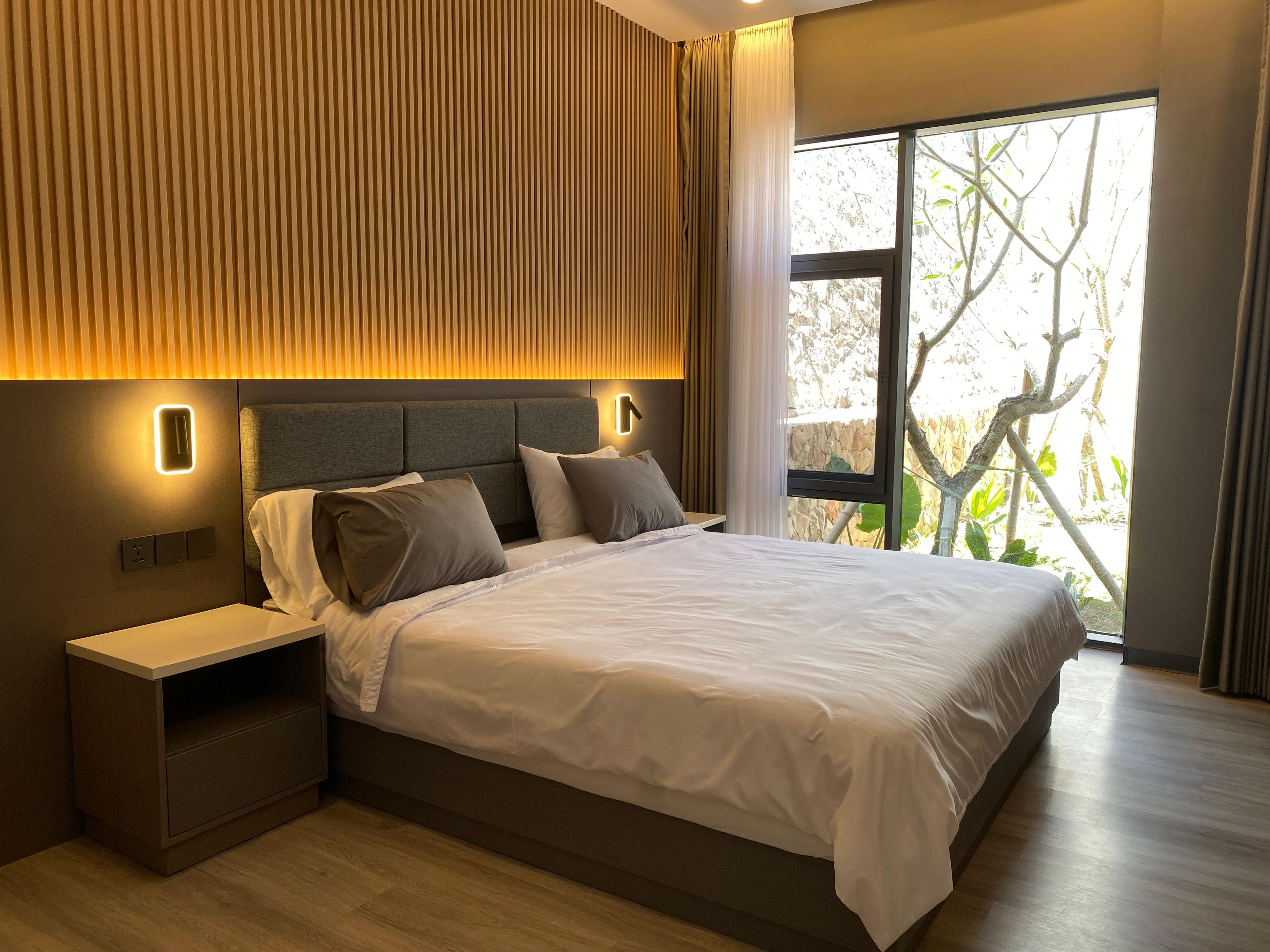 Un dormitorio moderno con una cama grande, mesitas de noche y vistas al verdor exterior.