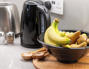 A kitchen counter with a bowl of fruit, a kettle, and a toaster. - J-Fitzrovia Skyhome | Spacious Central London 2BR (London)