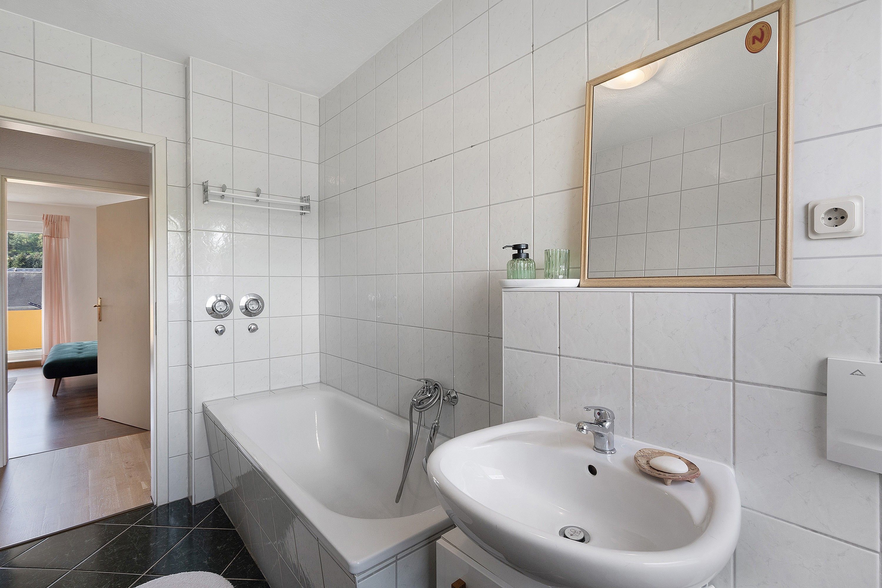 A bathroom with a bathtub, a sink, and a shower. There is a mirror on the wall and a towel rack.