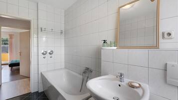 A bathroom with a bathtub, a sink, and a shower. There is a mirror on the wall and a towel rack.