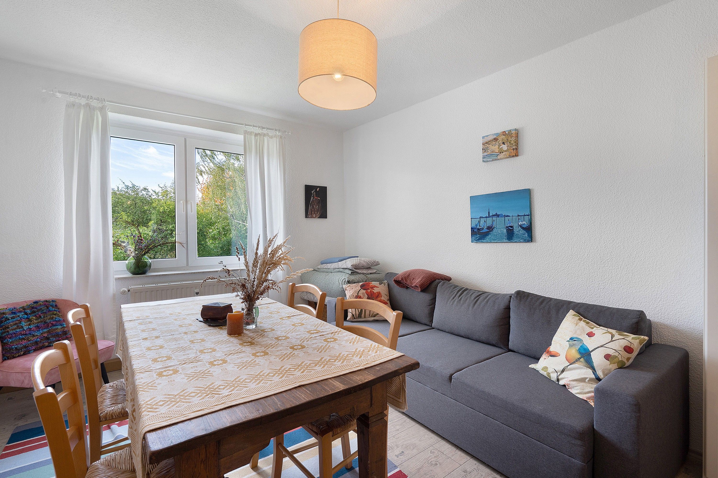 A cozy living room with a dining table, sofa, and artwork on the walls.