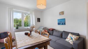 A cozy living room with a dining table, sofa, and artwork on the walls.