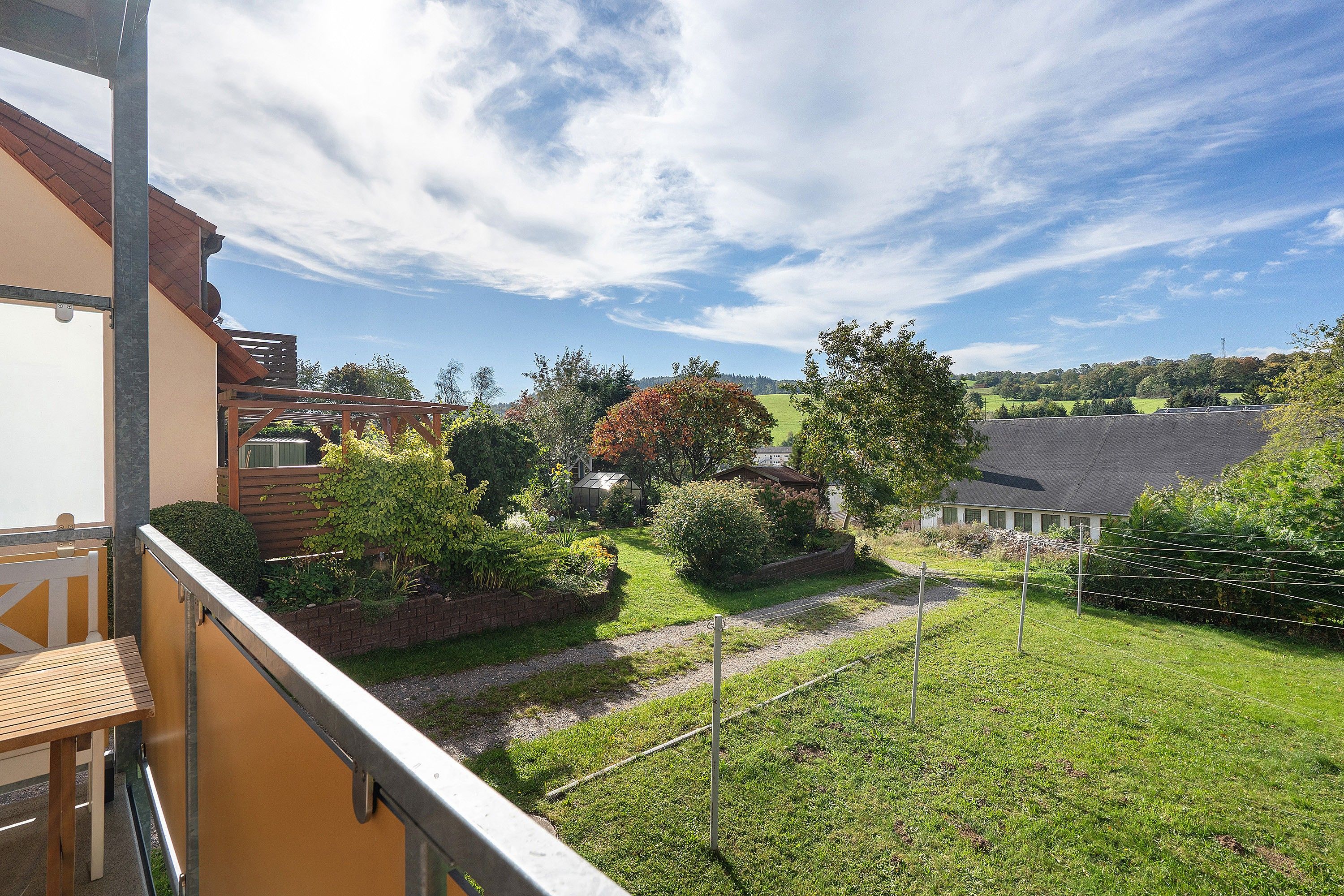 Ein Wohnhaus mit einem Balkon, der einen Garten und die umliegende Landschaft mit freiem Blick bietet.