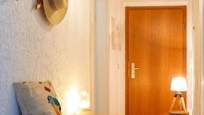 Ein Flur mit einer Holztür, einer Lampe, einem Wandhaken für Hüte und einer Bank mit Decke.