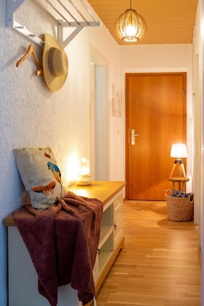 Un pasillo con puerta de madera, lámpara, perchero en la pared y un banco con manta.