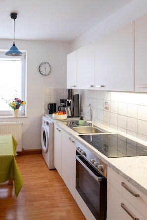 Una cocina moderna con armarios blancos, lavadora integrada, estufa y lavaplatos.