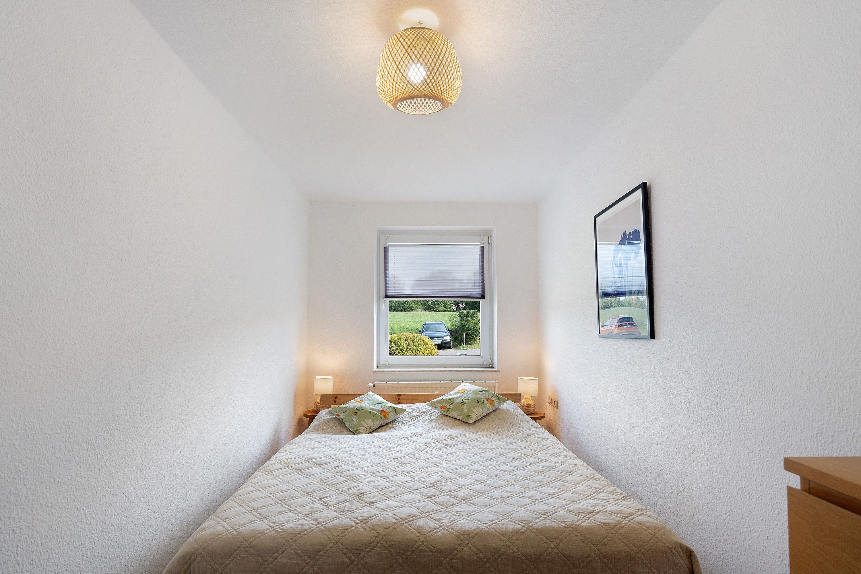 Ein Schlafzimmer mit einem Bett, einem Fenster, einem Wandbild und einer Deckenleuchte.