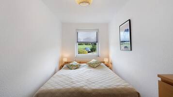 Ein Schlafzimmer mit einem Bett, einem Fenster, einem Wandbild und einer Deckenleuchte.