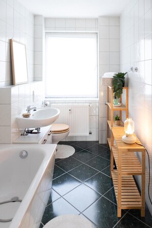 Un baño moderno con bañera, lavamanos, inodoro y ventana que proporciona luz natural.