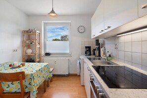 Une cuisine compacte avec un coin repas, un four encastré et une fenêtre équipée de stores.