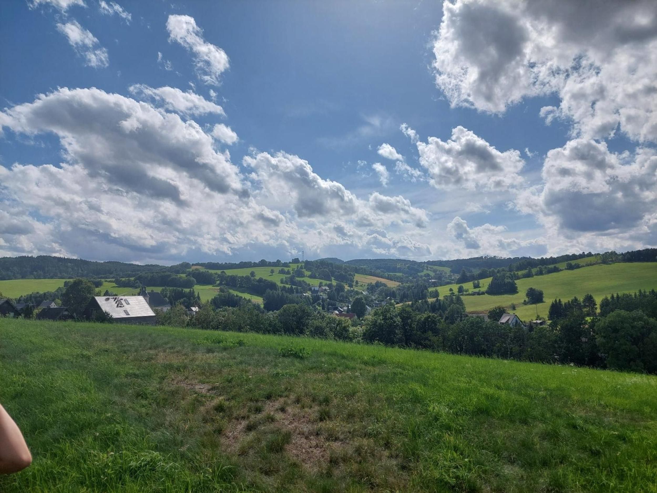 A rural landscape with rolling hills, scattered houses, and a clear sky with clouds.