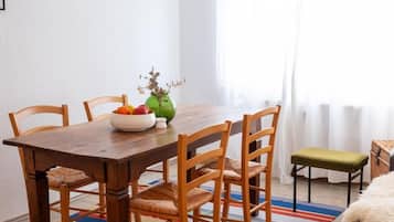 Ein Essbereich mit einem Holztisch, Stühlen, einer Blumenvase und einem farbenfrohen Streifen Teppich.