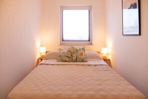Una cama con cubrecolcha acolchado, dos lámparas de noche y una ventana con persianas.