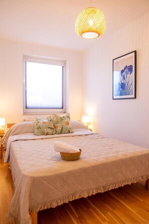 Un dormitorio con cama, ventana, lámpara de pared e imagen enmarco.