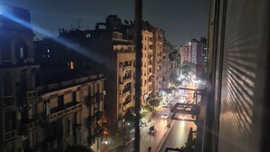 Een stadsgezicht 's nachts, zichtbaar vanuit een raam, met een straat vol voertuigen en verlichte gebouwen.