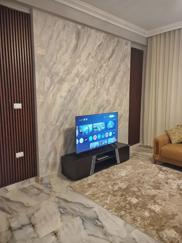A living room with a flat-screen TV on a stand, a brown leather sofa, and a marble-patterned floor. - 3BRs Garden City Lexus Living (Cairo Governorate)