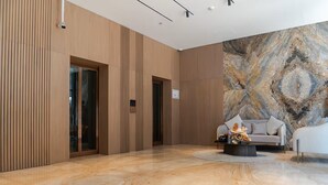 A modern lobby with a marble floor, a sofa, and a coffee table with a vase. - Vogue | PG One Al Furjan near Metro Station (Dubai)