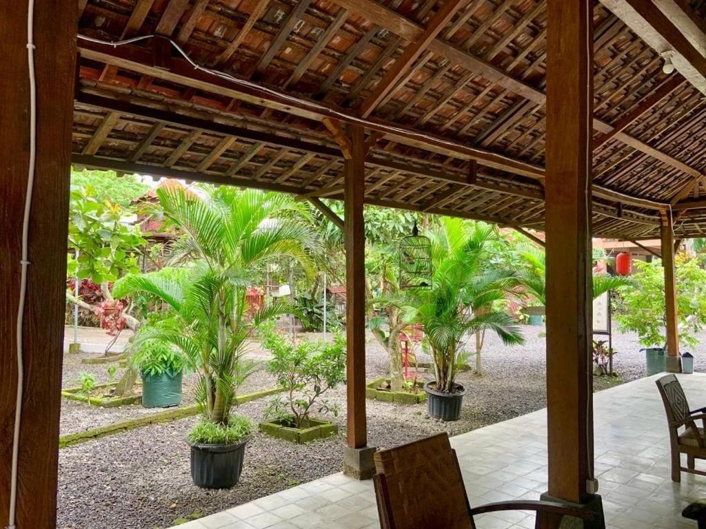 An outdoor covered area with wooden pillars, potted plants, and a tiled floor.