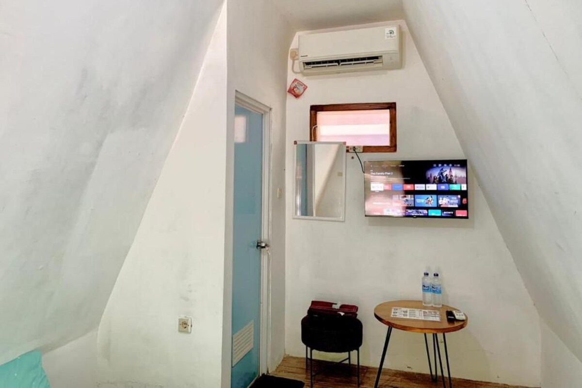 A small room with a sloped ceiling, a mounted TV, a small table with a chair, and an air conditioning unit.