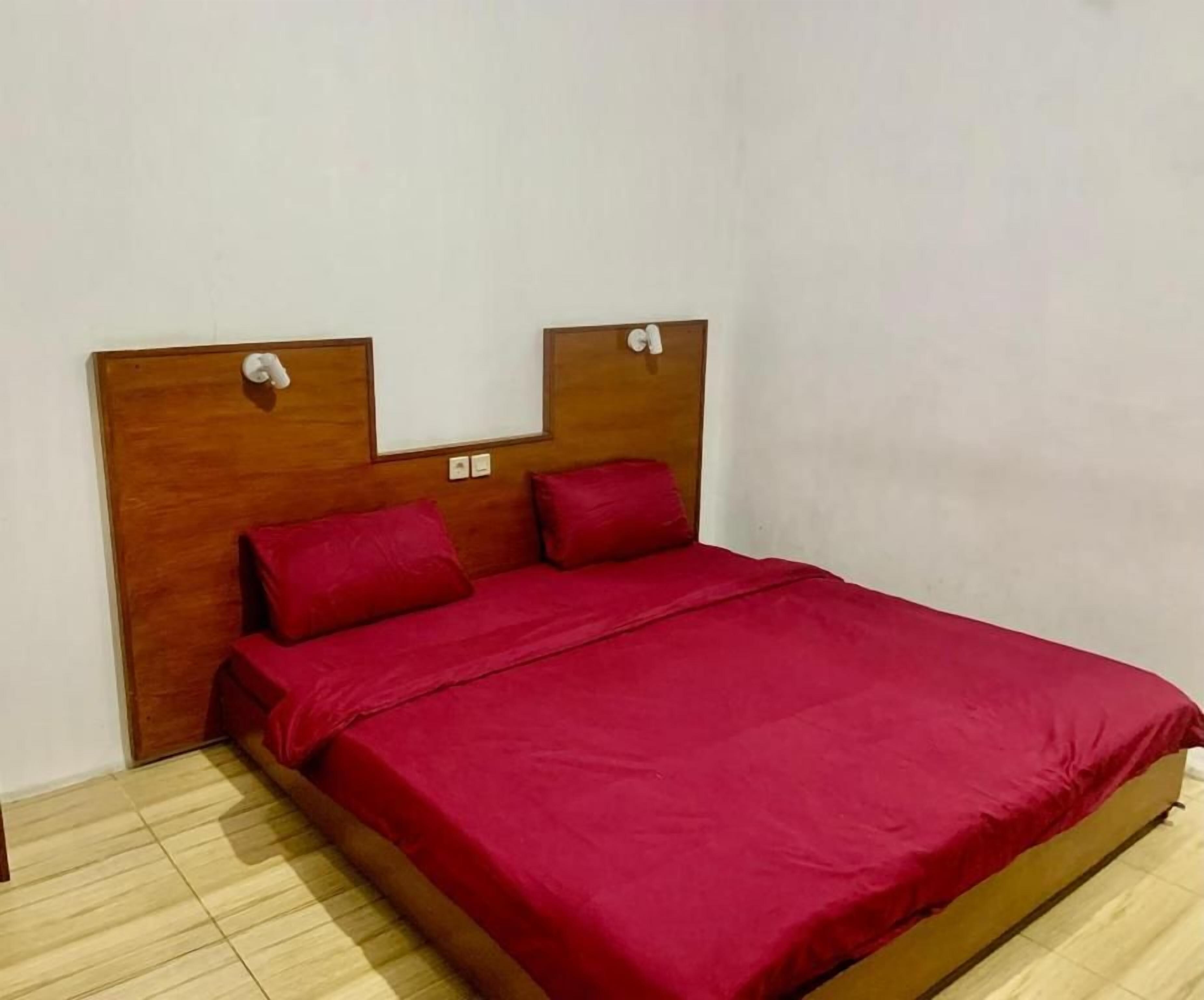A single-bed room with a wooden headboard, red bedding, and a light-colored wooden floor.