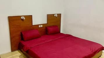 A single-bed room with a wooden headboard, red bedding, and a light-colored wooden floor.