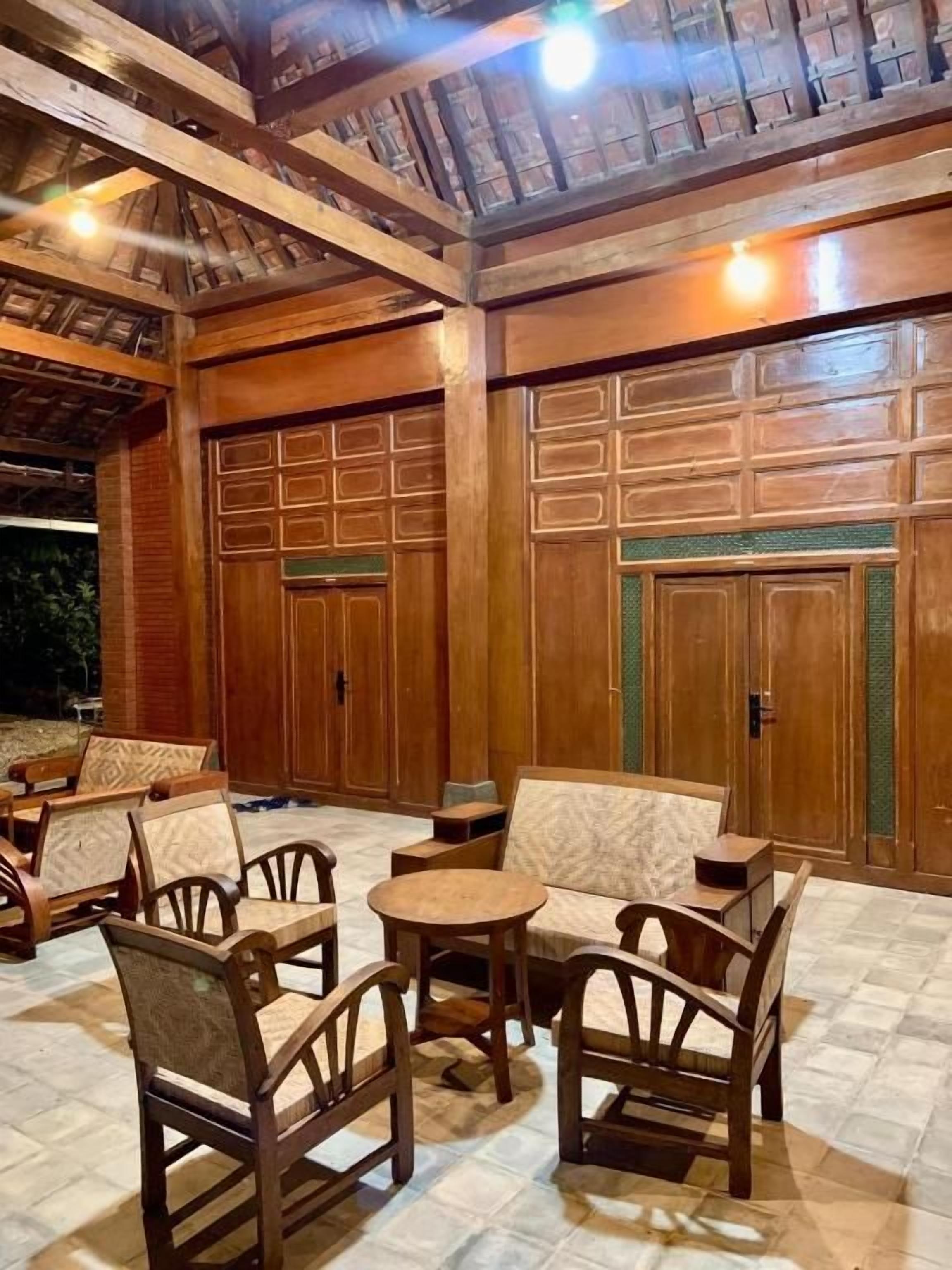 Un área de estar exterior con mobiliario de madera y piso de baldosas.