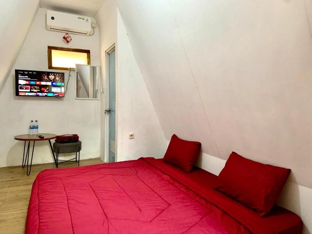 Una habitación con cama, televisor montado en la pared, una mesita con silla y equipo de aire acondicionado.