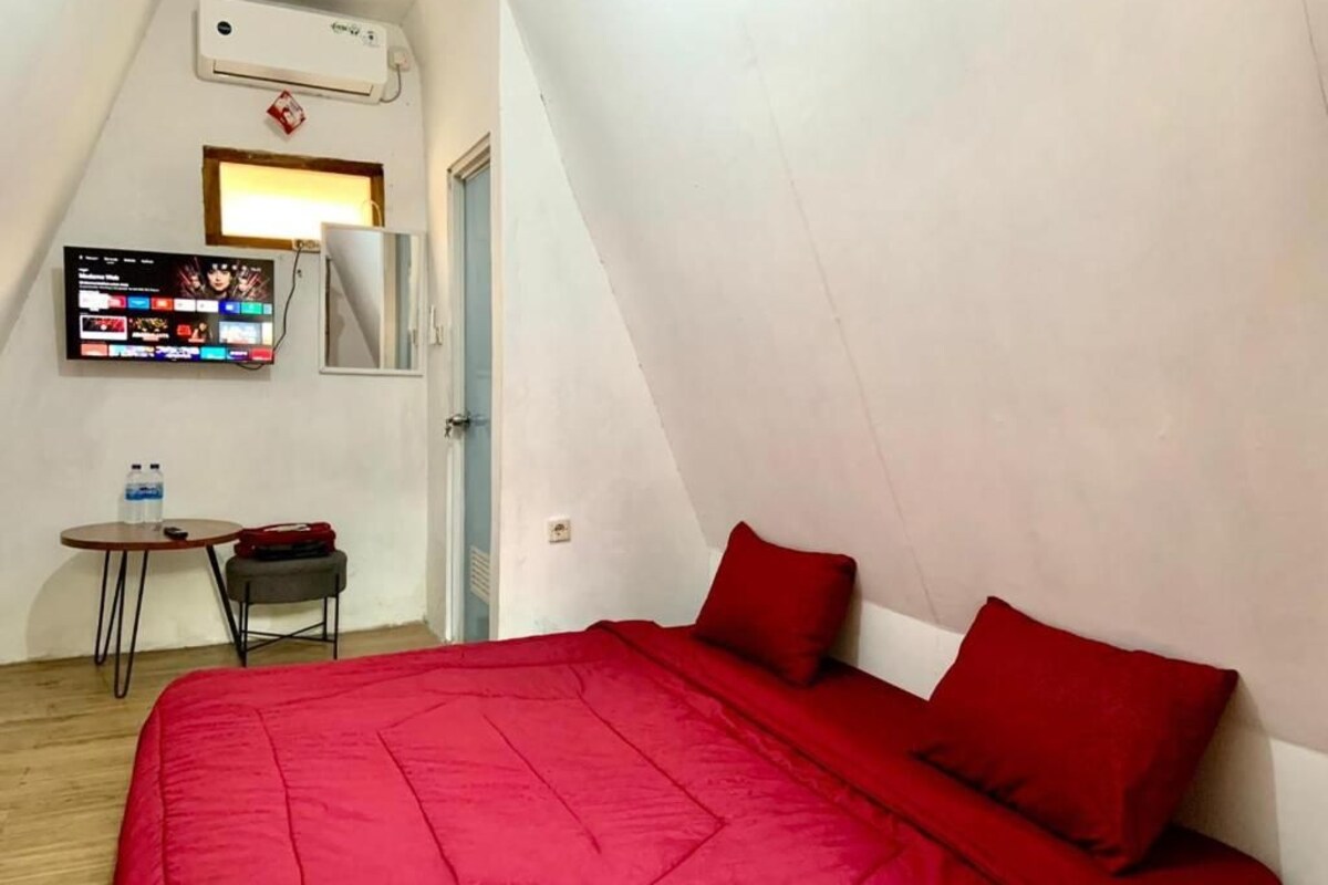 Una habitación con cama, televisor montado en la pared, una mesita con silla y equipo de aire acondicionado.