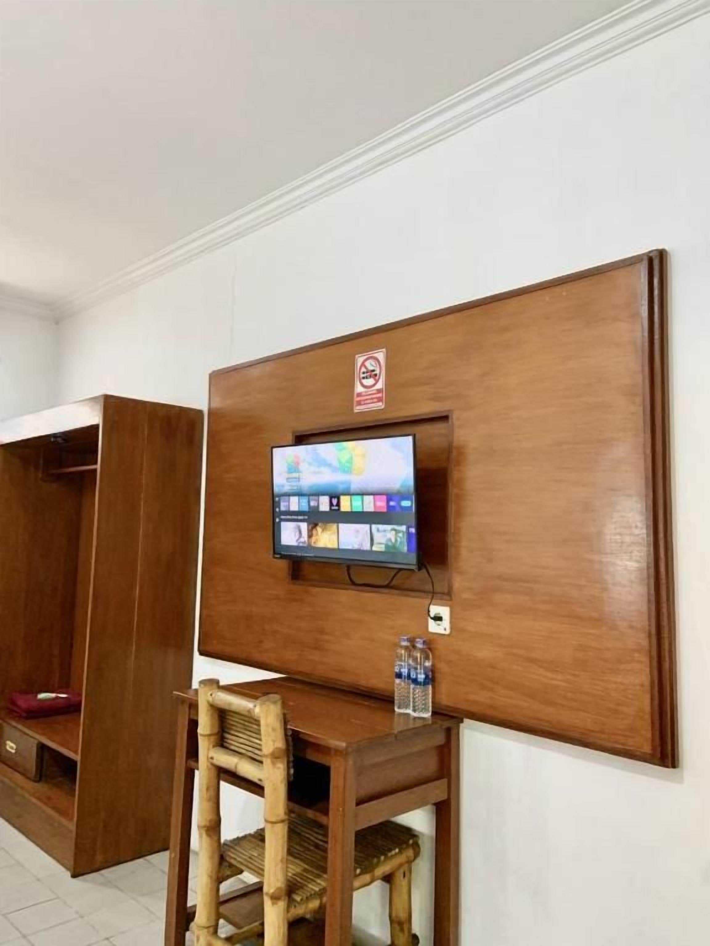 A room with a wooden panel wall, a mounted television, a wooden desk with a chair, and a water bottle on the desk.