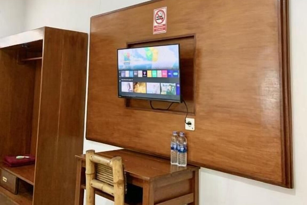 A room with a wooden panel wall, a mounted television, a wooden desk with a chair, and a water bottle on the desk.