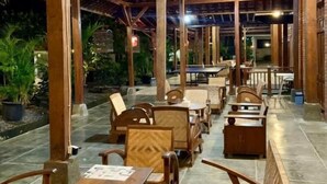 An outdoor seating area with wooden tables and chairs, a covered roof structure, and potted plants. - Sokkyo Homestay Kaliurang (DI Yogyakarta)