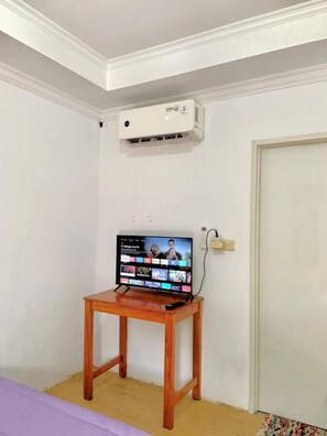 Una habitación con una cama, una mesa de madera con un televisor, un equipo de aire acondicionado y una puerta.