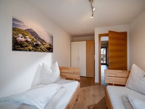 Quarto com duas camas, um guarda-roupa de madeira e uma porta que dá para outro cômodo.