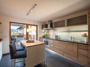 Cozinha moderna com ilha central, armários de madeira, eletrodomésticos de aço inoxidável e iluminação pendente.