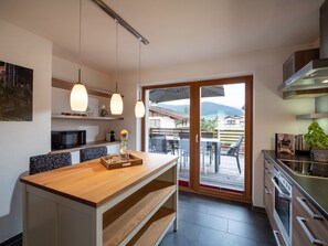 Eine moderne Küche mit einer Holzinsel, Pendelleuchten und Blick auf einen Balkon mit Gartenmöbeln.